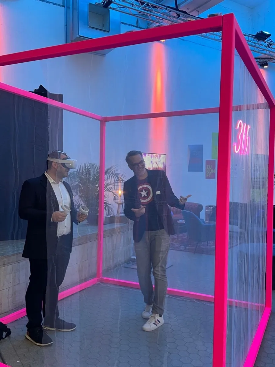 Zwei Personen testen eine VR-Brille in einem leuchtenden Würfel